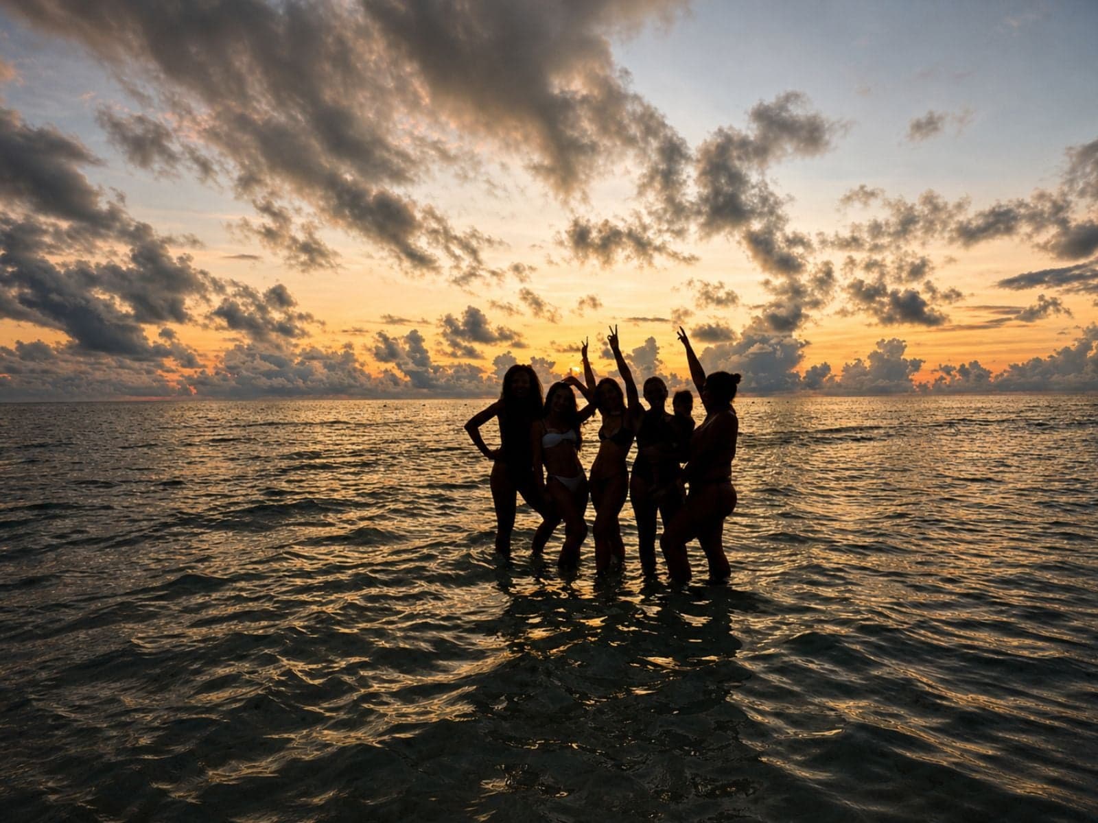 Group of friends celebrating in the sea at sunrise, backlit