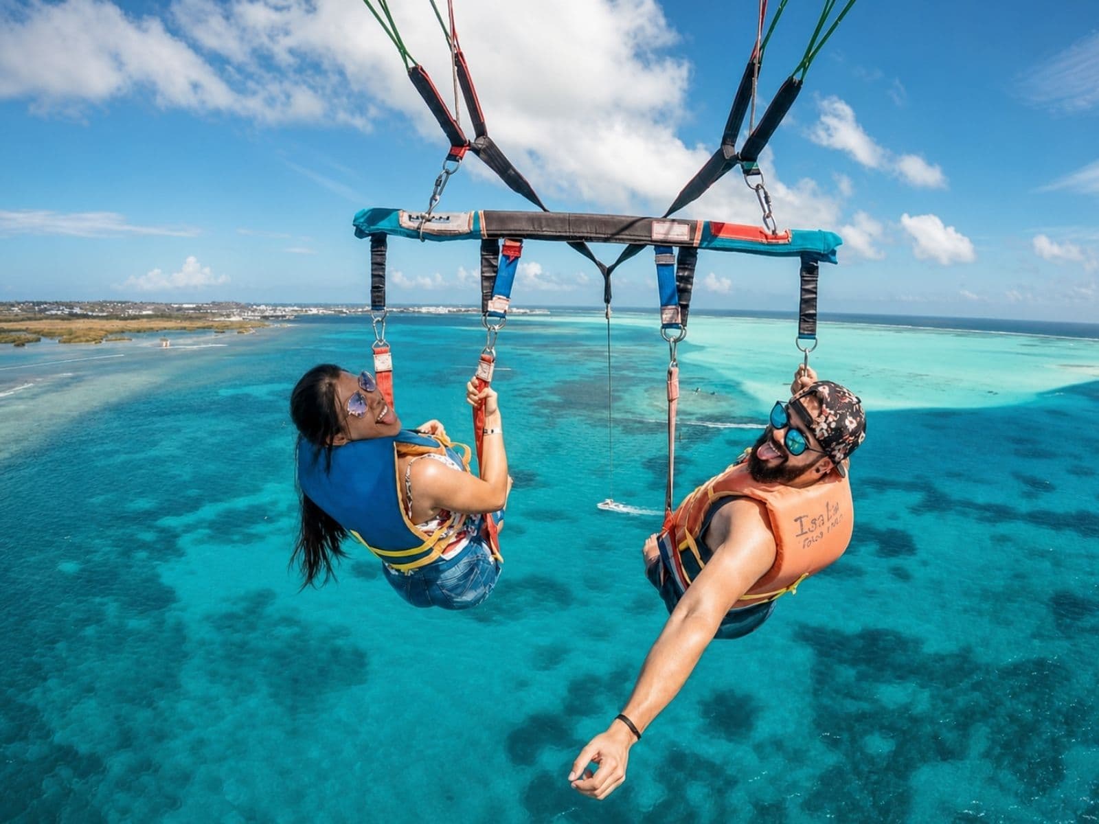 A couple mid-flight, each in their own harness, over the turquoise sea