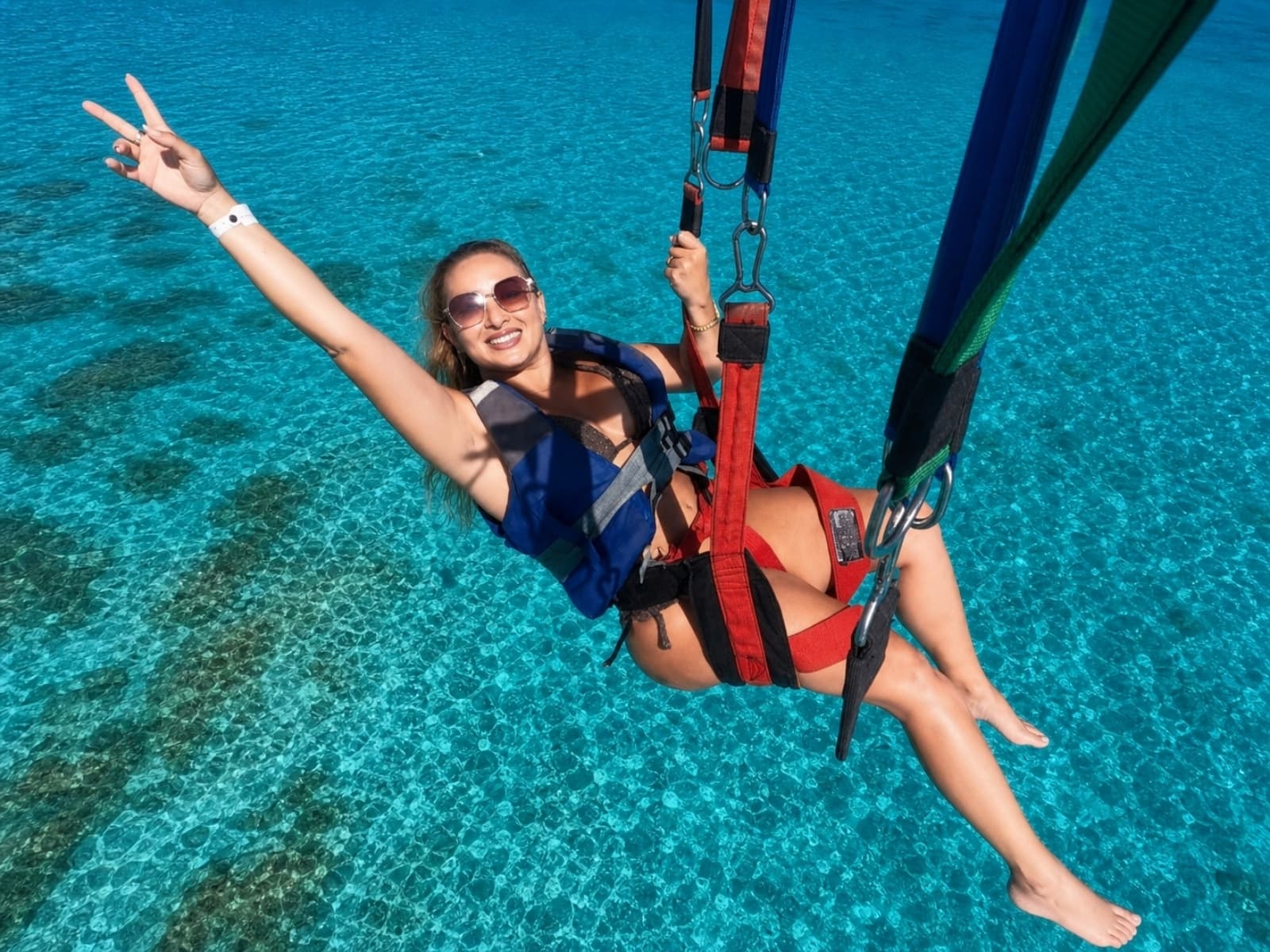 A traveler with her arm raised parasails over the turquoise waters of the reef