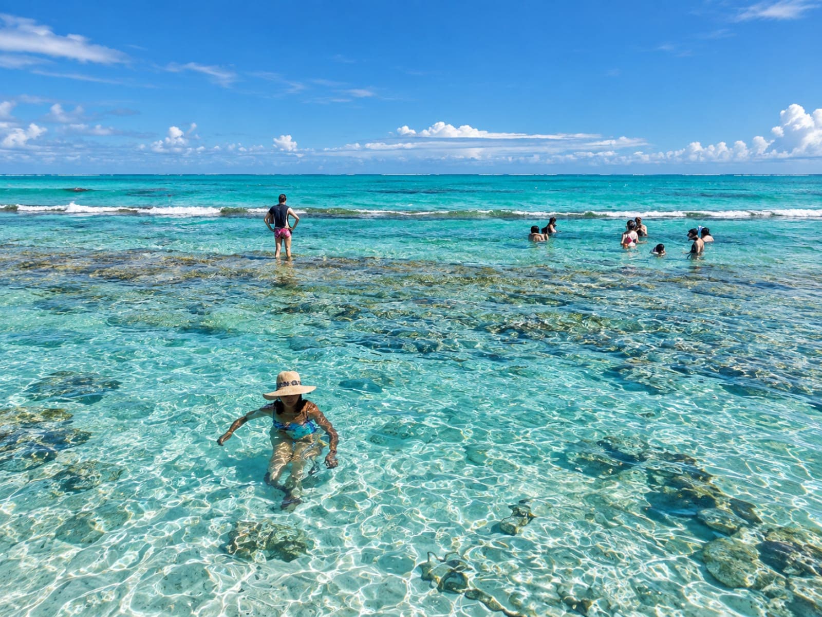 Traveler in a hat sitting in the crystal-clear, shallow water, over the coral bottom