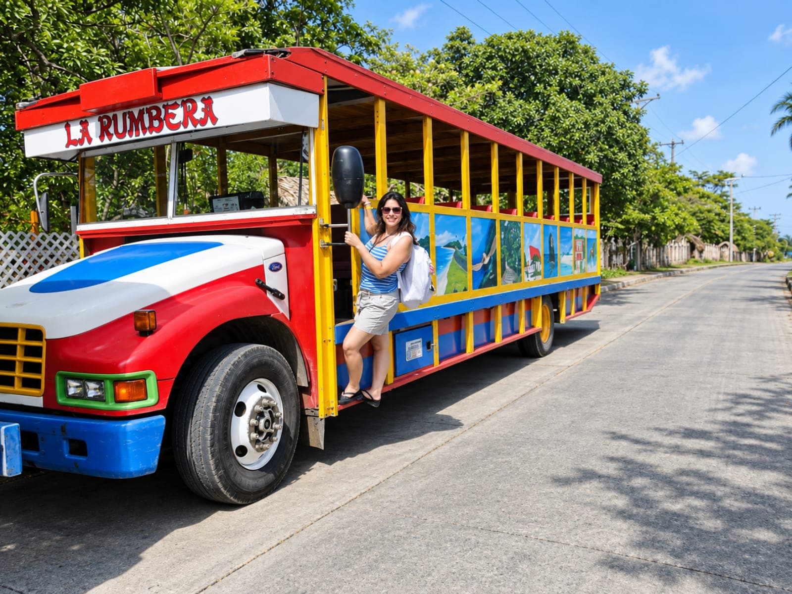 Smiling traveler standing on the step of the red, white, blue and yellow “La Rumbera” chiva bus, with island landscapes painted on its sides